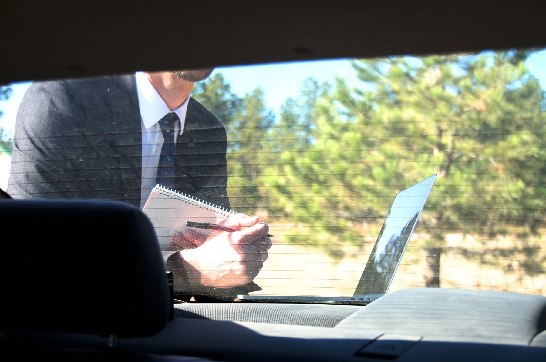 Police officer reviewing notes through cruiser back window with laptop on trunk