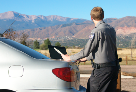 Officer beside cruiser with laptop on trunk and mountains in the distance